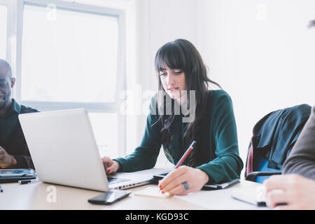 Junge schöne kaukasischen Geschäftsfrau sitzt auf dem Schreibtisch mit Computer - Technologie, arbeiten, Business-Konzept Stockfoto