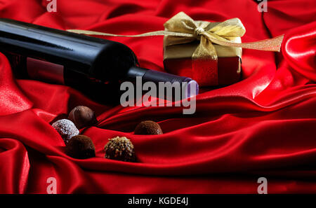 Valentines Tag Konzept. rote Flasche Wein, Pralinen und einem Geschenkkarton auf roter Seide Textil Stockfoto