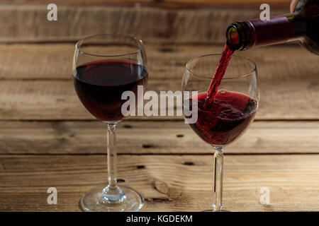 Gießen Rotwein in einem Glas auf einem Holztisch Stockfoto