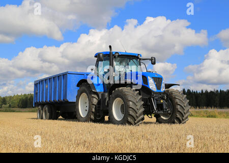 Somero, FINNLAND - 12. SEPTEMBER 2015: New Holland T 7,250 Traktor und blauer landwirtschaftlicher Anhänger auf Stoppelfeld. New Holland feiert 12 Jahrzehnte Stockfoto