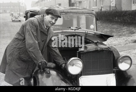 1950, historische, am frühen Morgen und ein Herr tragen ein Mantel, Mütze und Handschuhe ist auf der Straße vor seinem Haus mit der Motorhaube seines Autos zurück gefaltet und auf der Fahrerseite öffnen, England, UK. Stockfoto