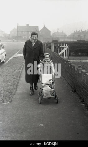 1950, historische, Mutter eingepackt in Mantel und Schal heraus gehen mit ihrer jungen Tochter, drückt eine kleine Kinderwagen oder Buggy der Ära mit ihren kleinen Puppe, die mit einer Decke, England, UK gewickelt ist. Stockfoto