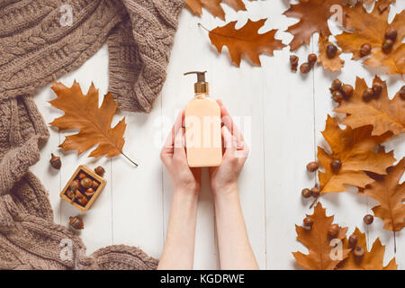 Flasche mit flüssiger Seife in weibliche Hände auf weißem Hintergrund aus Holz mit einem weichen Tuch und Eichenlaub. Blick von oben. Das Konzept von Schönheit und Pflege f Stockfoto