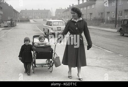 1950, historische, Mutter, die mit ihrem kleinen Kind und Baby im Kinderwagen in der Nähe der lokalen Geschäfte des Rates bezüglich einer Wohnsiedlung, England, UK. Stockfoto