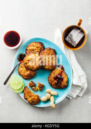 Cookies mit Erdnussbutter und Marmelade auf einem blauen Schild auf einen weissen Stein Hintergrund und Tasse Tee Stockfoto