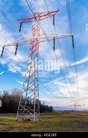 Hohe Spannung der elektrischen Freileitungen und Masten mit blauem Himmel und einige Wolken im Hintergrund. Stockfoto