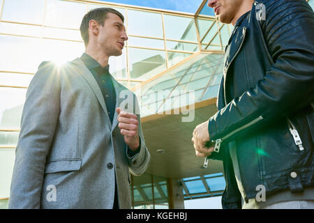 Low Angle Portrait von zwei schöne und erfolgreiche Männer sprechen im Freien außerhalb der modernen Bürogebäude stehend, lens flare Stockfoto