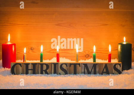 Das Wort Weihnachten aus Holz Buchstaben in künstlichen Schnee mit Kerzen brennen und eine hölzerne Hintergrund. Stockfoto