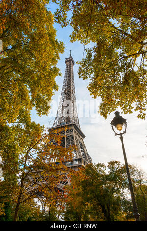 Low Angle Blick auf den Eiffelturm durch das Laub der Bäume im Herbst mit einer alten Straße Licht im Vordergrund. Stockfoto