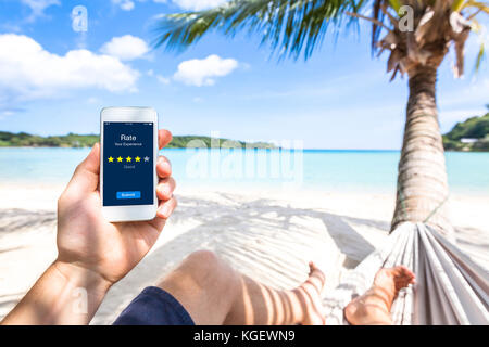 Customer Review online App auf dem Smartphone Display Benutzer am Strand Erfahrungen zu bewerten und Feedback, zufriedenheit Bewertung mit star Symbole geben Stockfoto