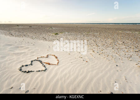 Pebbles angeordnet in Form von zwei Herzen auf Sand strand Wellen Stockfoto