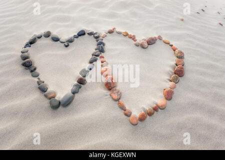 Pebbles angeordnet in Form von zwei Herzen auf Sand strand Wellen Stockfoto