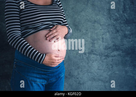 Freundliche, liebevolle Schwangere mit den Händen auf ihren Bauch im dritten Trimenon der Schwangerschaft erwarten neugeborenes Baby Stockfoto