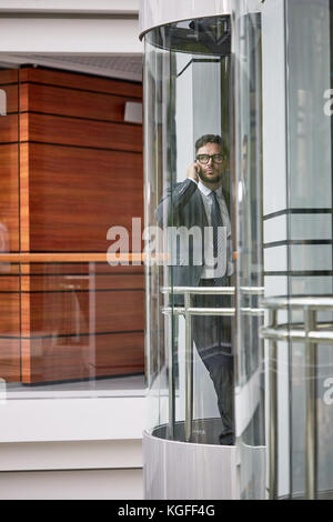 Volle Länge Portrait von zuversichtlich im mittleren Alter Unternehmer tragen von klassischen Anzug Durchführung Telefon Verhandlungen mit Business Partner beim Gehen Stockfoto