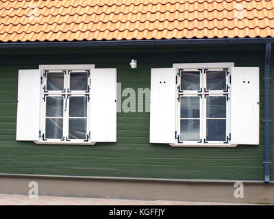 Zwei Retro Stil weiß Holzfenster mit Rollläden auf grünem Holz- Haus Wand- und roten Lehm Ziegeldach Stockfoto