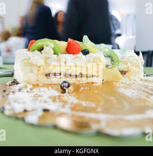 In Scheiben geschnitten Kuchen mit frischem Obst auf Kuchen board gekrönt mit Menschen im Hintergrund Stockfoto