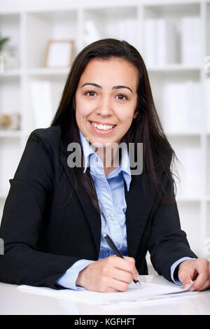 Porträt einer jungen, fröhlichen Geschäftsfrau, die im Büro auf dem Schreibtisch sitzt Stockfoto