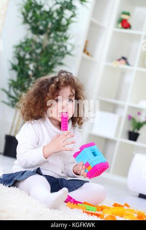 Lustige kleine Mädchen spielen mit Bau Blöcke, holding Block im Mund Stockfoto