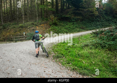 Ein Mountainbiker sein Mountainbike hochdrücken, einem steilen Track im Cardinham Holz in Cornwall. Stockfoto