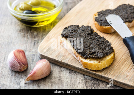 Schwarze Oliven Tapenade mit Sardellen, Knoblauch und Olivenöl in Toast auf hölzernen Tisch Stockfoto