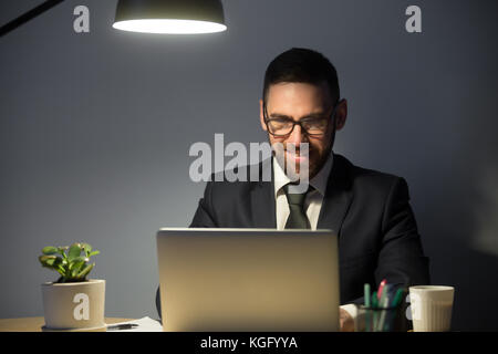 Junger erwachsener Mann in Brille, der spät nachts am Laptop arbeitet. Mann, der am Abend auf der Arbeit ein Video-Chat-Vorstellungsgespräch für eine Position in einer abgelegenen Stadt macht Stockfoto