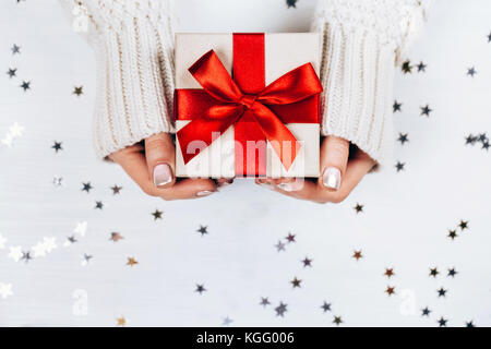 Weibliche Hände halten Geschenk mit roter Schleife Stockfoto