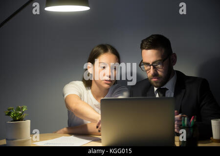 Zwei schwere Kollegen arbeiten auf ein Problem am späten Abend treffen. weiblichen Trainer zeigen männliche Mitarbeiter wichtige Projektdetails in Laptop s Stockfoto