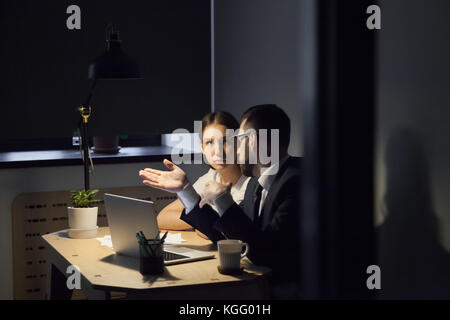Zwei Kollegen diskutieren in einer Besprechung am späten Abend über das neue Projekt. Männlicher Coach zeigt weibliche Mitarbeiter wichtige Details auf dem Laptop-Bildschirm. Stockfoto