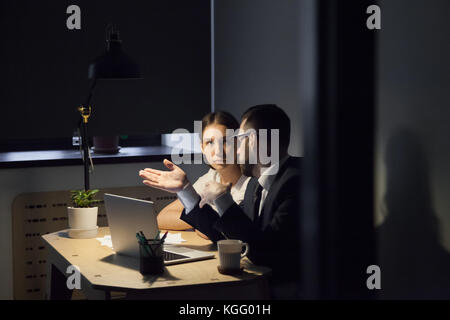 Zwei Kollegen diskutieren neues Projekt am späten Abend treffen. männliche Trainer zeigen weibliche Mitarbeiter wichtige Details im Laptop. Stockfoto