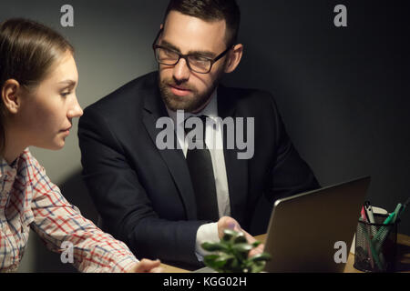 Superior erklären Junge untergeordnete wichtigsten Punkte am späten Abend treffen erlebt. männliche Trainer aufmerksam betrachten Studentin versucht, Stockfoto