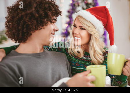 Porträt der jungen glückliches Paar feiert Weihnachten zu Hause entspannen mit Tassen Tee auf einem Sofa in einer Wohnung. Stockfoto