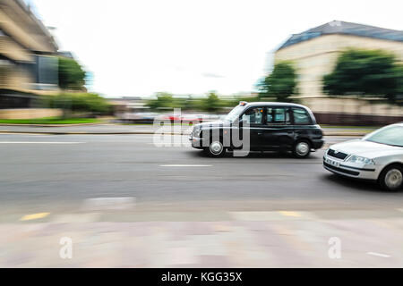 Foto von schwarzen Taxi Auto und Silber Auto schnell auf einer Straße gehen, gleiche Richtung von rechts der Photo Frame links. in Glasgow auf overcas Stockfoto