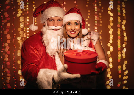 Schöne junge lächelnde Paar in santa claus Kostüm mit roten vorhanden und Kamera. Stockfoto