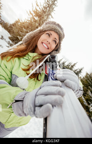 Schöne junge Frau genießen im Skiurlaub. Sie stehen mit Skiern und weg schauen mit Lächeln. Stockfoto