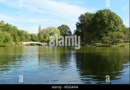 Bogen Brücke über den See im Central Park an einem sonnigen Tag. Touristen und Einheimische auf dem Gras- und Ruderboote auf dem Wasser entspannen. Stockfoto