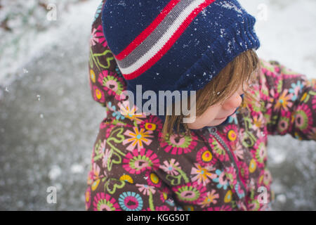 Ein Kleinkind steht außerhalb der Kleidung tragen im Winter mit Schnee um sie herum. Stockfoto