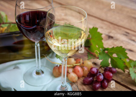 Rot- und Weißwein Gläser und frischen Weintrauben auf hölzernen Hintergrund, auf dem Glas Wein konzentrieren Stockfoto
