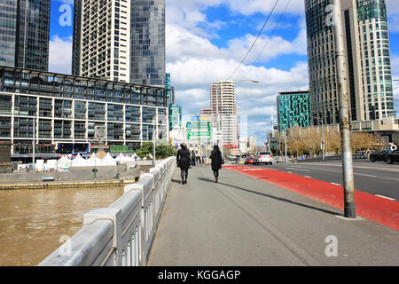 Zwei weibliche junge Erwachsene gehen auf eine Brücke über den Fluss Yarra in Melbourne, Australien, Ansicht auf einem Wolkenkratzer Stockfoto