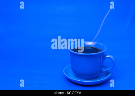 Blauer Becher mit dampfendem heißem Kaffee. Weicher Rauch. Blauer Hintergrund. Horizontales Foto mit Platz zum Schreiben Stockfoto