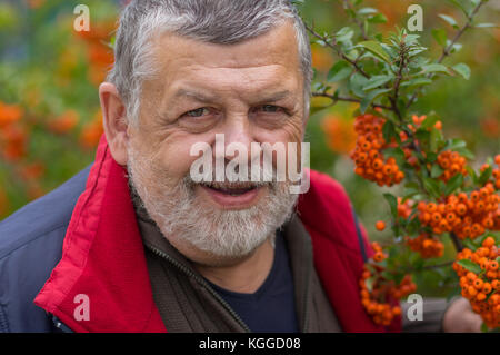 Outdoor Portrait von älteren Menschen gegen Strauch mit orangefarbenen Beeren im Herbst Garten Stockfoto