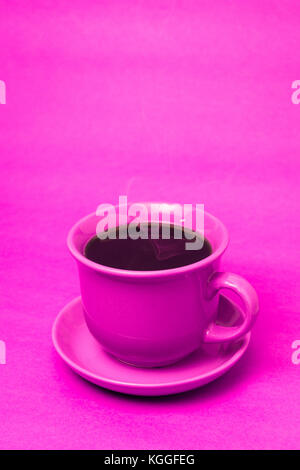 Rosa Tasse mit dampfenden heißen Kaffee. Weicher Rauch. Pinker Hintergrund. Vertikales Foto mit Platz zum Schreiben Stockfoto