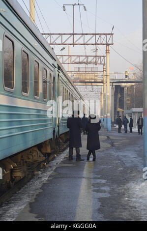 Russischer Zug in Kasachstan im Winter, Menschen, die auf dem Bahnsteig gehen und aus dem Zug aussteigen. Zug Dirigent, prowodnik, mit uschanka, Pelzhut. Stockfoto