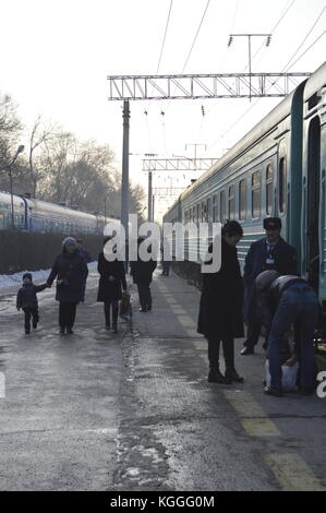 Russischer Zug in Kasachstan im Winter, Menschen, die auf dem Bahnsteig gehen und aus dem Zug aussteigen. Zug Dirigent, prowodnik, mit uschanka, Pelzhut. Stockfoto