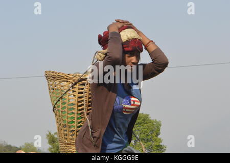 Nepalesische Frau, die einen Strohkorb mit einem Kopfband auf ihrem Kopf trägt, in einem kleinen Dorf in Bacheck, Nepal. Stockfoto