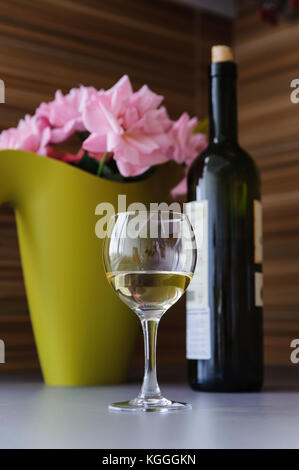 Blumen, eine Flasche und ein Glas Weißwein auf dem Tisch. Stockfoto