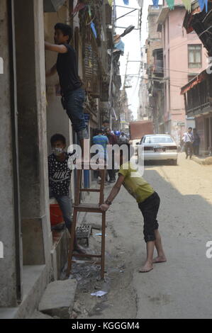 Drei nepalesische Jungen arbeiten. Eine befindet sich auf einer Leiter und zwei stützen und halten die Leiter. Straßenszene, Kathmandu, Nepal. 1y nach dem Erdbeben Stockfoto