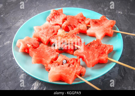 Wassermelone in Form von Sternen auf Spieße liegt auf einer Platte. Die blaue Teller ist wie eine Rakete im Weltraum. top View Stockfoto