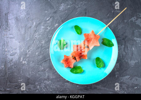 Wassermelone in Form von Sternen auf Spieße mit Blättern der Minze liegt auf einem blauen Platte. top View Stockfoto