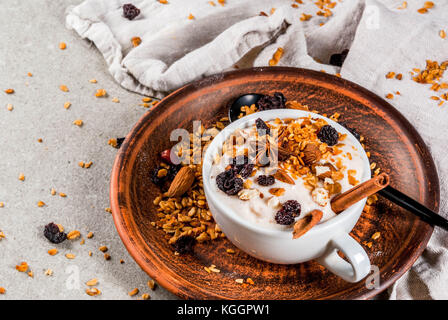 Ideen für einen Herbst Winter Frühstück. würzig Joghurt mit Müsli, getrocknete Früchte, Nüsse, Mandeln, Gewürze (Zimt, Anis), in der Schale, auf Platte. grau Hinterg Stockfoto