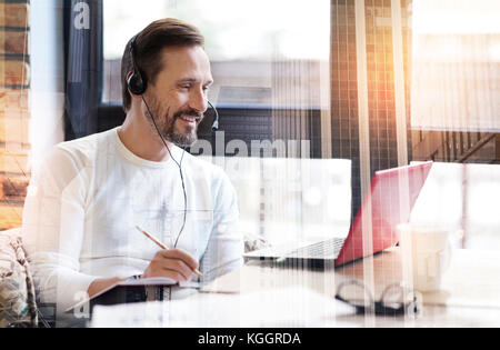 Fröhlicher junger Mann in Webinar teilnehmen und sich Notizen Stockfoto